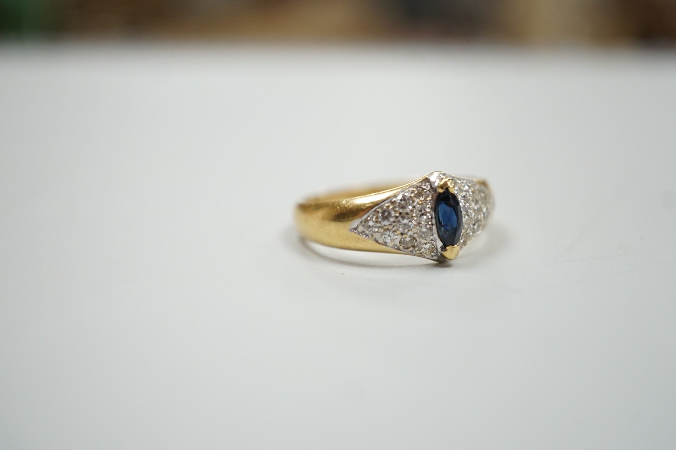 A modern 18ct gold and single stone marquise cut sapphire set dress ring, with pave set diamond shoulders, size R, gross weight 5 grams.